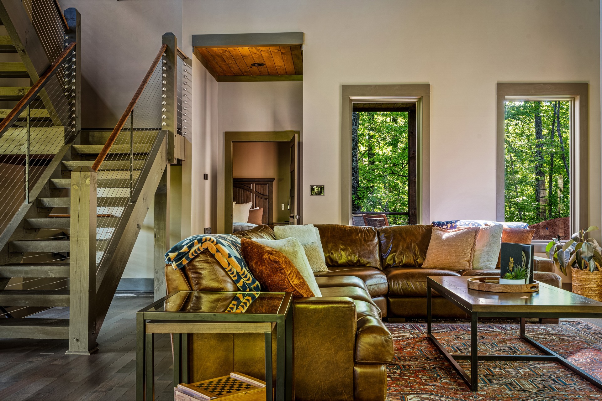 Spacious living room with leather sectional, open staircase and forest views