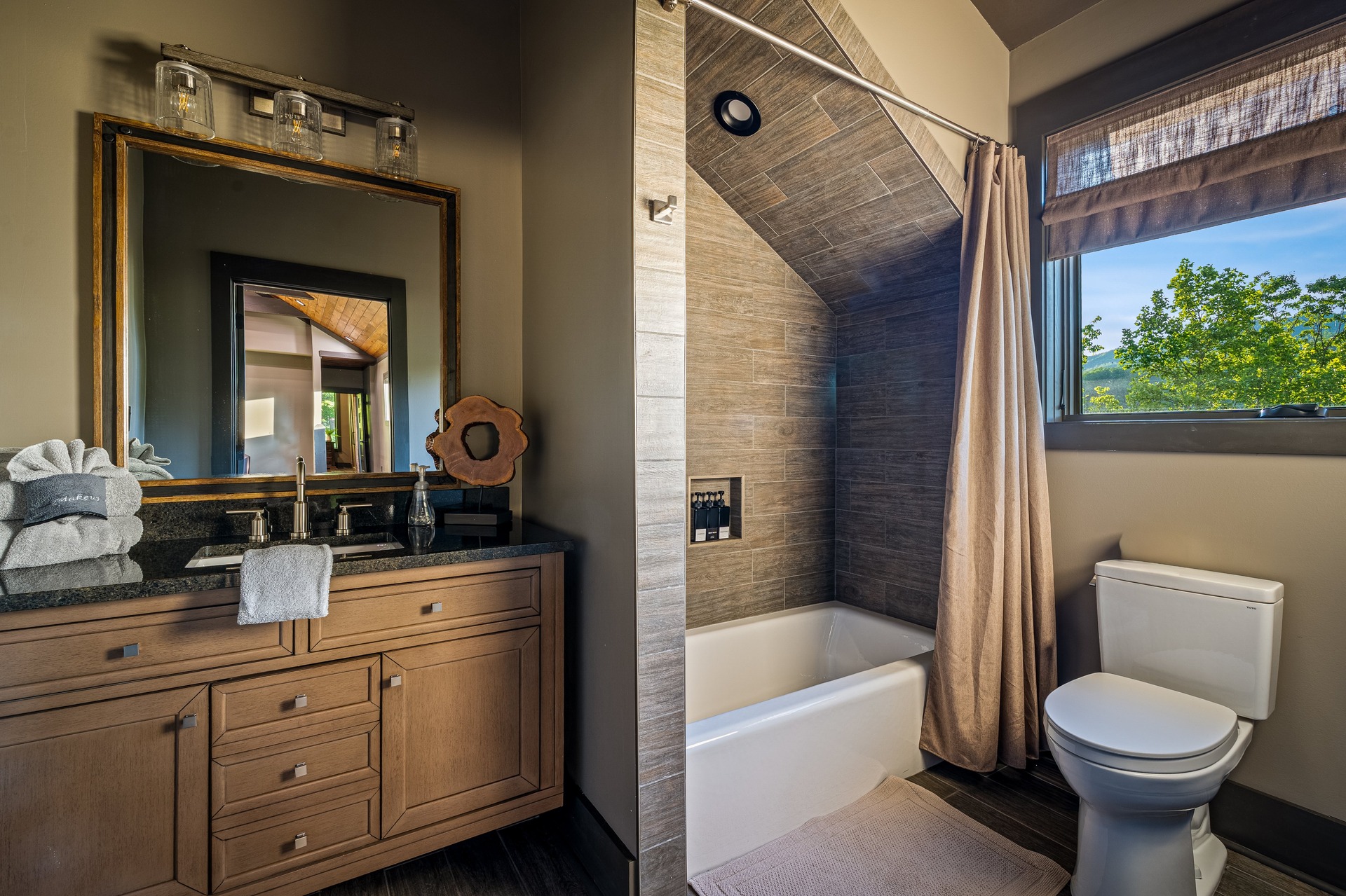 Bedroom 3 bathroom with wood vanity, tiled tub and forest-view window