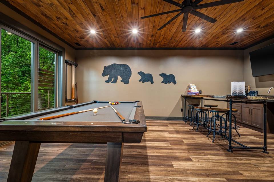 Game room with pool table, bar seating, forest and seasonal mountain views.