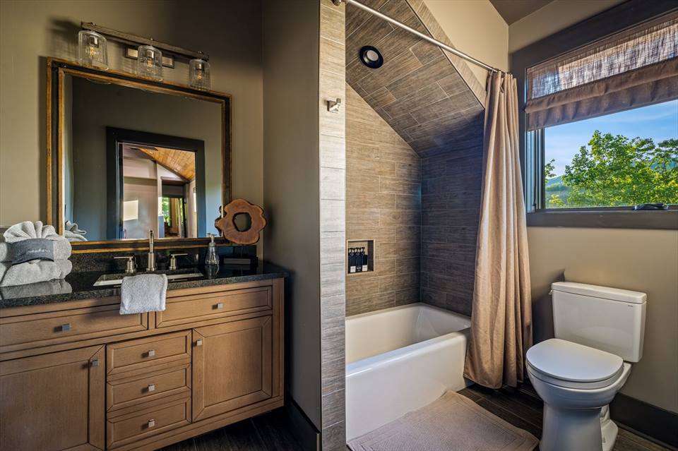 Bedroom 3 bathroom with wood vanity, tiled tub and forest-view window