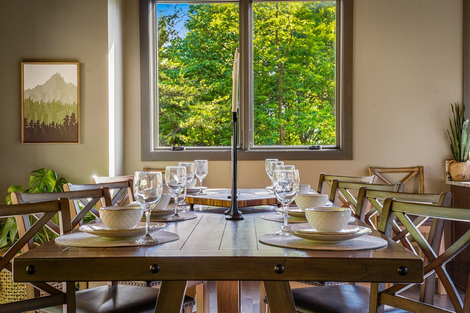 Dining room table set for a meal beside large forest-view windows